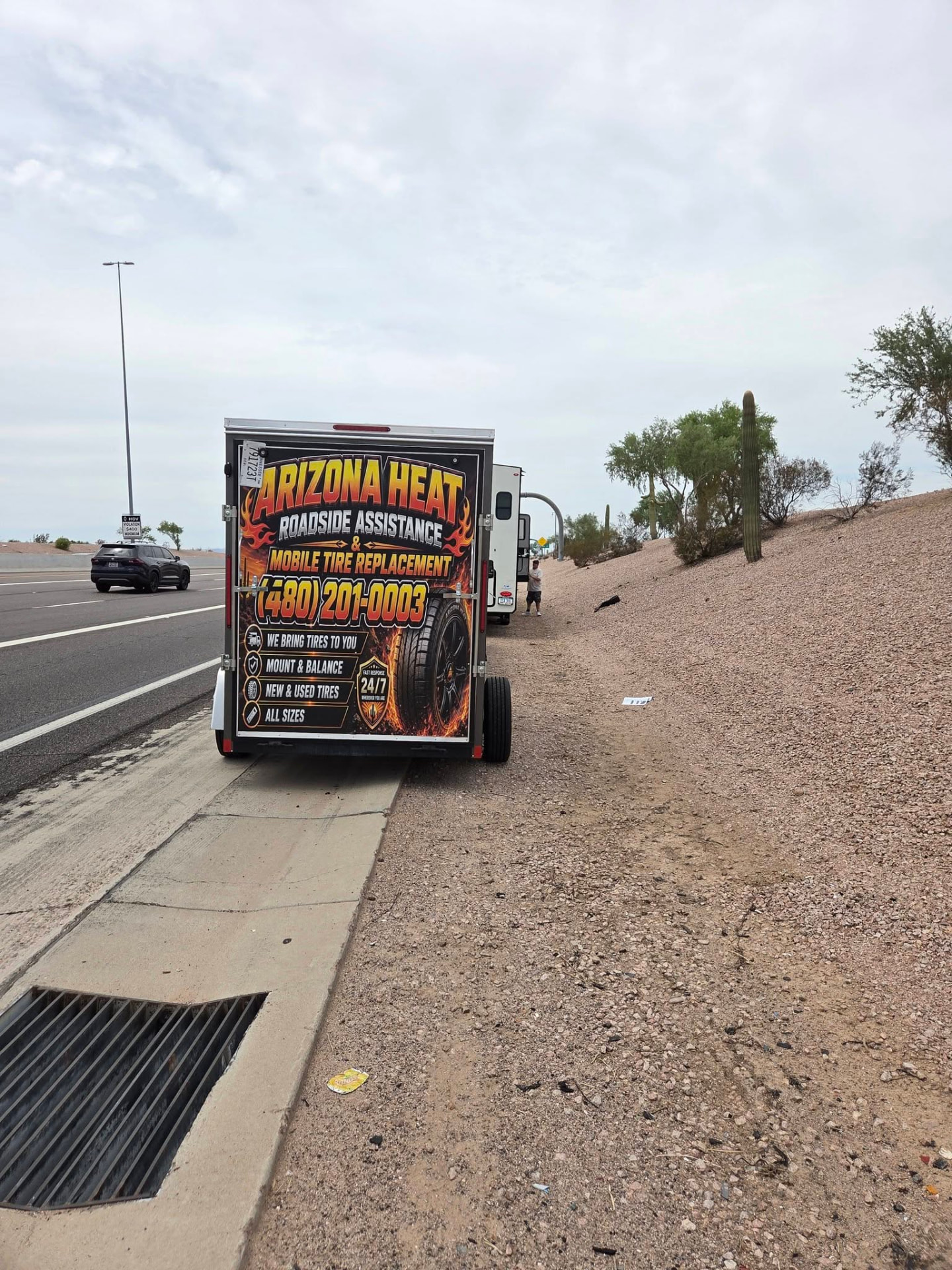 Roadside assistance technician standing beside a service truck with amber warning lights on an Arizona road